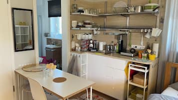 Una cuina compacta amb zona de menjador, armaris blancs i una finestra petita.