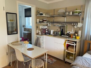 Cocina compacta con comedor, muebles blancos y una ventana pequeña.