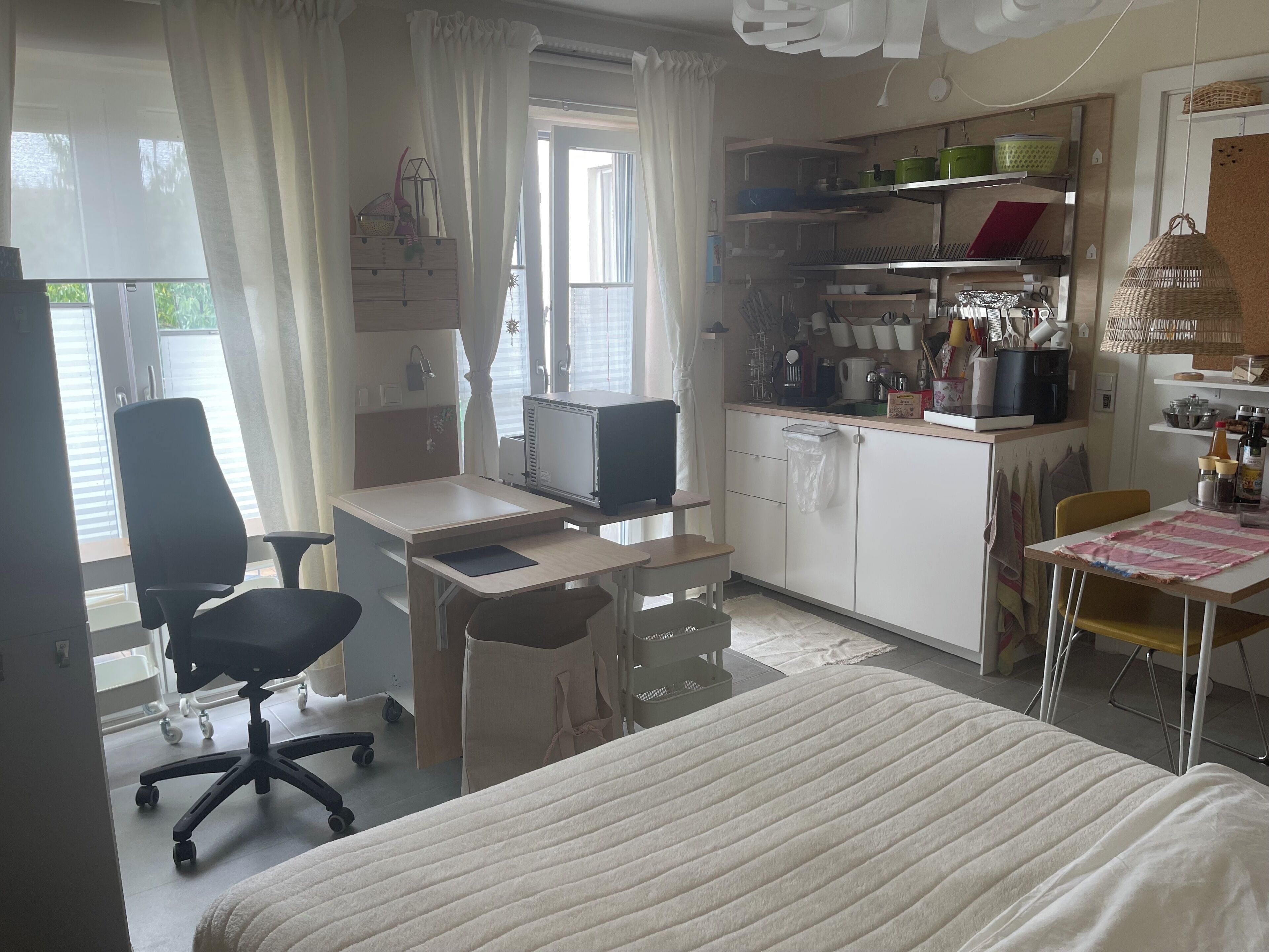 A compact room with a bed, a desk with a computer, a chair, and a kitchenette area.