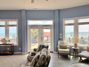 A room with a large window offering a view of the beach, a sofa, a chair, and a small table. - Turtle Cottage: 3BR 2BA, Oceanfront, Rooftop Deck, Gazebo, Sleeps 7 (Oak Island)