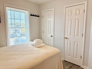 A bedroom with a bed, a coat rack, and a door. - Turtle Cottage: 3BR 2BA, Oceanfront, Rooftop Deck, Gazebo, Sleeps 7 (Oak Island)