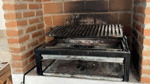 Un barbecue extérieur en briques, doté d’une grille en métal, d’une étagère inférieure et d’une pile de bois de chauffage en dessous.