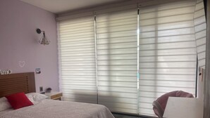 Une chambre à coucher comprenant un lit, une table de chevet, une chaise et une fenêtre avec des stores.