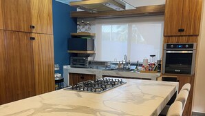 Une cuisine moderne dotée d’un îlot en marbre, d’un four encastré et de meubles de rangement en bois.
