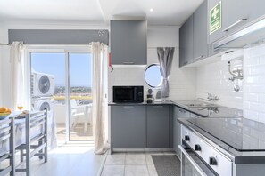 A modern kitchen with grey cabinets, a black microwave, and a window overlooking a cityscape. - #415 Charming Apartment | Albufeira (Albufeira)