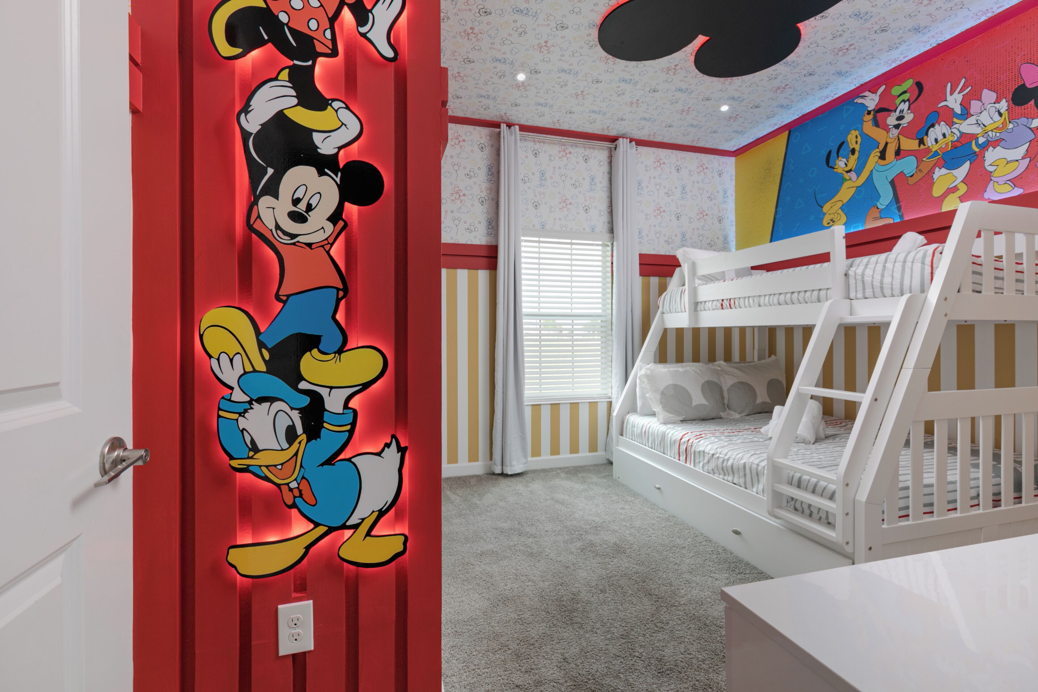 Ein Kinderzimmer mit Etagenbett, Wandbildern von Mickey Mouse und Donald Duck sowie einem Fenster mit Jalousien.
