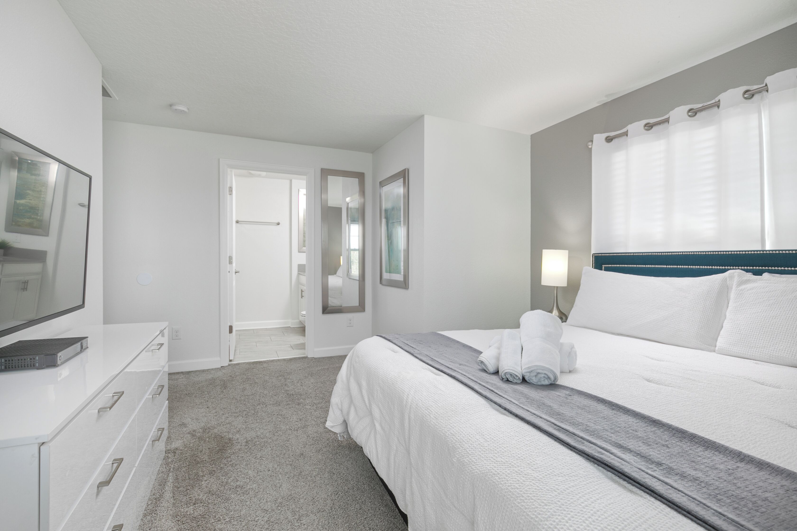 A hotel room with a bed, a TV, a desk, and a bathroom visible through an open door.