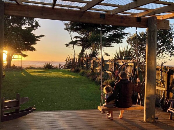 Una terraza de madera con un columpio, un espacio cubierto con vista al océano y un jardín.