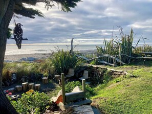 Un jardín costero con un banco de madera, una escultura de ave y vista al mar.