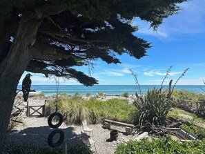 Eine Strandansicht mit Baum, Schaukeln aus Reifen und einer Bank.