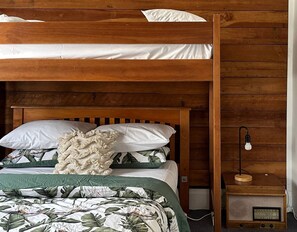 Una cama litera con cabecera de madera, una radio sobre una mesita auxiliar de madera y una colcha estampada.
