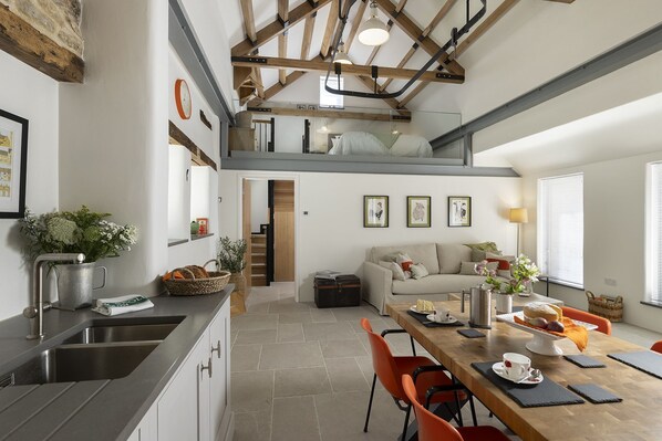 A modern kitchen with a dining area, a staircase leading to an upper level, and a view of the outside. - The Old Abattoir -  an apartment that sleeps 2 guests  in 1 bedroom (Chipping Campden)