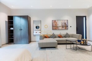 Ein modernes Wohnzimmer mit Sofa, Hocker, Couchtisch, einem Kleiderschrank und Kunstwerken an der Wand.