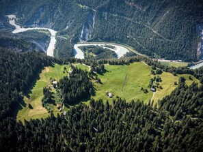 An aerial view of a mountainous area with a river, forested slopes, and scattered buildings.
