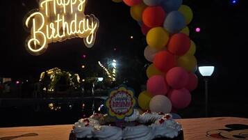 A birthday cake with a 'Happy Birthday' topper, surrounded by balloons and a neon sign in the background.