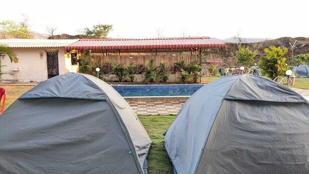 Two tents set up near a swimming pool with a building in the background.