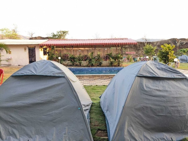 Two tents set up near a swimming pool with a building in the background.