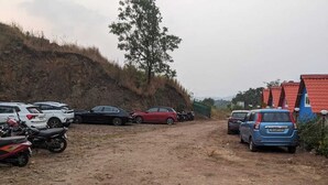 A dirt road leading to a parking area with several cars and motorcycles.