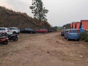 A dirt road leading to a parking area with several cars and motorcycles.