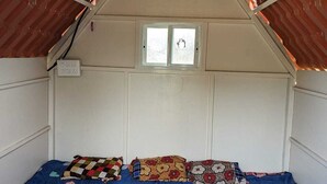 A bedroom with a sloped ceiling, a bed with a blue bedspread featuring heart patterns, and a window with a view of the outside.