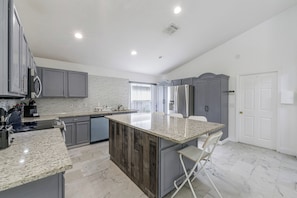 A modern kitchen with grey cabinets, a granite countertop, and a built-in island with seating. - Poolside Fun 8 Mi to Disney! Family Getaway (Kissimmee)