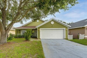 A residential house with a green exterior, a white garage door, and a driveway leading to the entrance. - Poolside Fun 8 Mi to Disney! Family Getaway (Kissimmee)