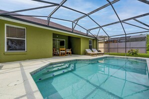 A swimming pool with a clear blue water, surrounded by a covered patio area with lounge chairs and a table. - Poolside Fun 8 Mi to Disney! Family Getaway (Kissimmee)
