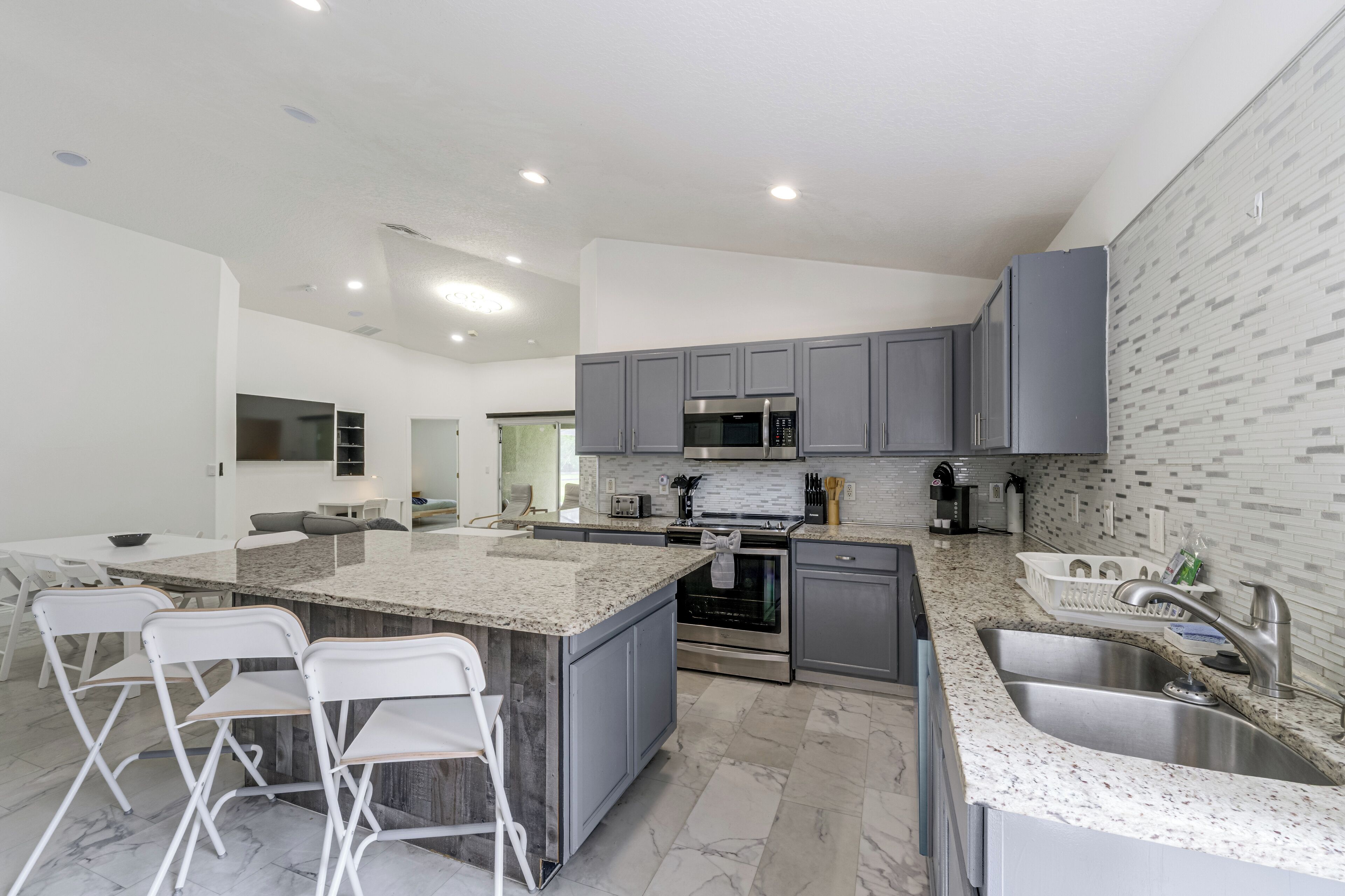 Una cocina moderna con gabinetes grises, una isla central con taburetes de bar, electrodomésticos de acero inoxidable y un salpicadero de azulejos.