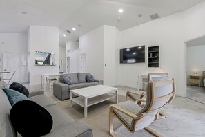 A modern living room with a sofa, coffee table, and a wooden rocking chair. - Poolside Fun 8 Mi to Disney! Family Getaway (Kissimmee)