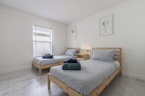 A bedroom with two wooden beds, a window with blinds, a bedside table with lamps, and a wall-mounted light fixture. - Poolside Fun 8 Mi to Disney! Family Getaway (Kissimmee)