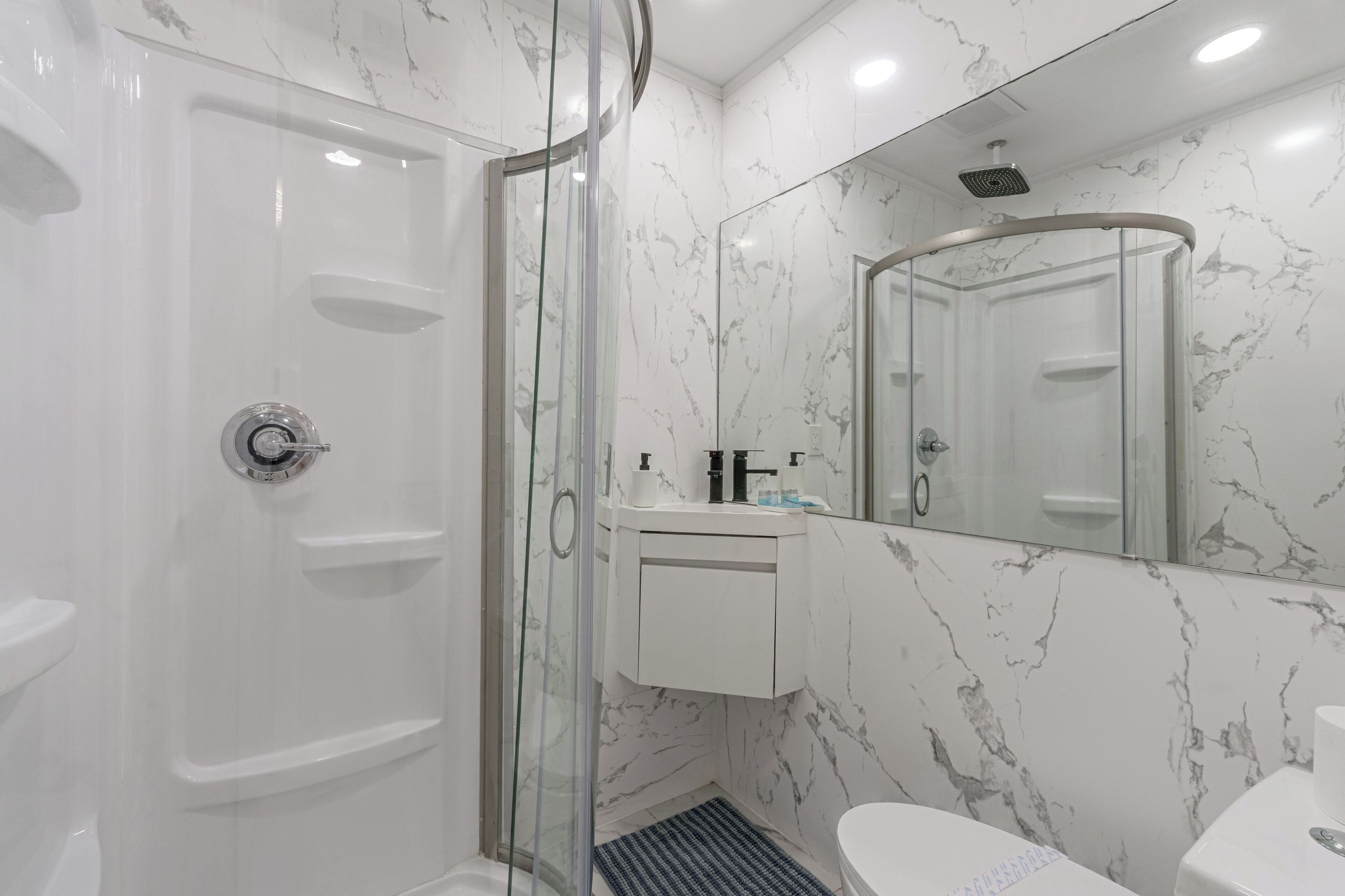 A modern bathroom with a glass-enclosed shower, a white sink, and a large mirror.