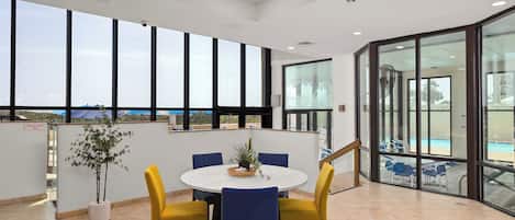 Un espace intérieur spacieux avec une table ronde et des chaises, de grandes fenêtres et une vue sur une piscine.