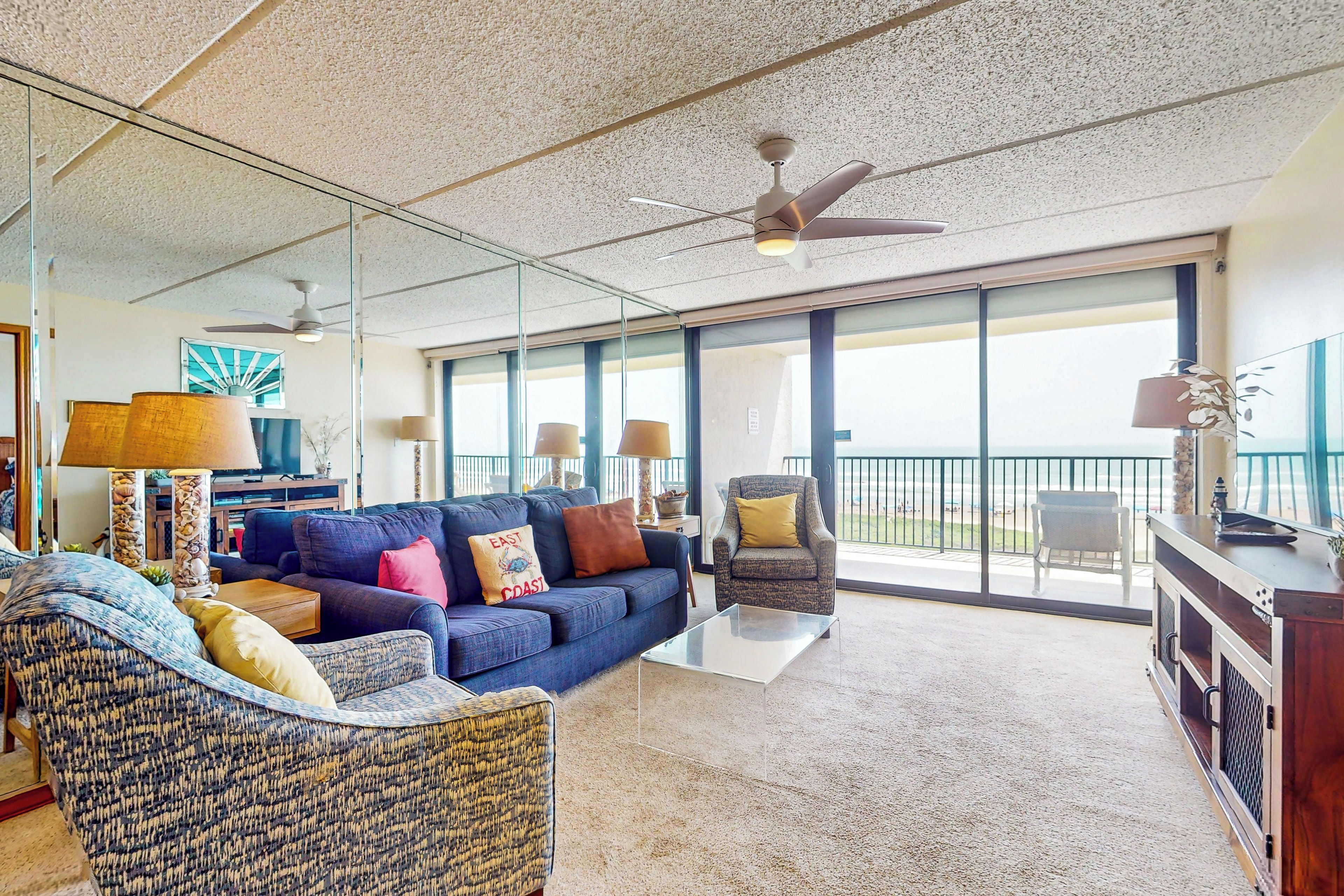 Un amplio salón con un sofá grande, un sillón estampado y un balcón con vistas.