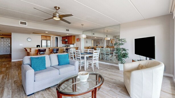 A spacious living area with a sofa, a glass coffee table, a white armchair, a TV, and a dining area in the background. - All-suite 3br, Gulf Views: Suntide III - Unit 208 (South Padre Island)