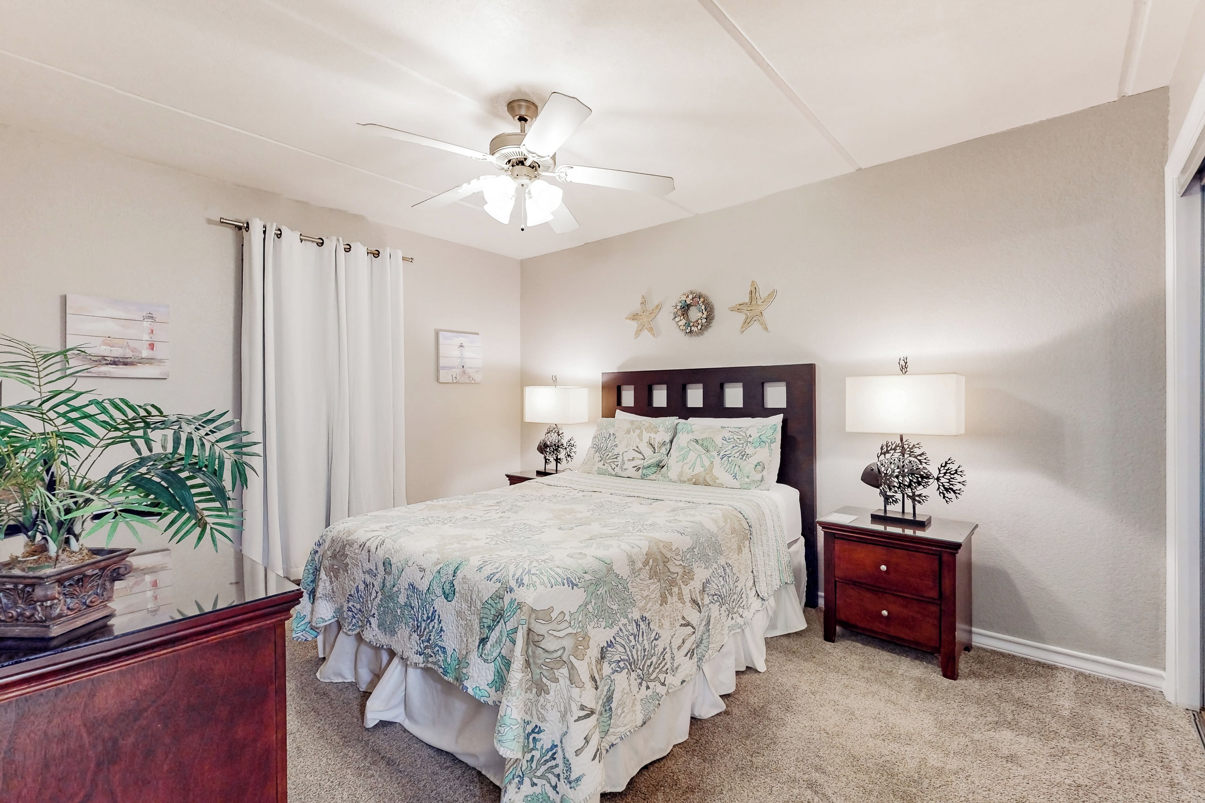 A bedroom with a bed, two bedside tables, a ceiling fan, a potted plant, and a wall with two starfish decorations.