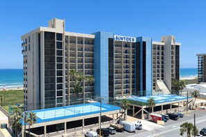 Ein mehrgeschossiges Hotel mit blauer und weißer Fassade, genannt 'SUNTIDE III', mit Poolbereich auf dem Dach und einem Parkplatz mit mehreren Fahrzeugen.
