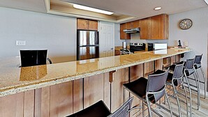 A modern kitchen with a central island, bar stools, stainless steel appliances, and wooden cabinetry. - All-suite 3br, Gulf Views: Suntide III - Unit 208 (South Padre Island)