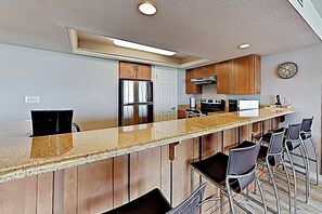 A modern kitchen with a central island, bar stools, stainless steel appliances, and wooden cabinetry. - All-suite 3br, Gulf Views: Suntide III - Unit 208 (South Padre Island)