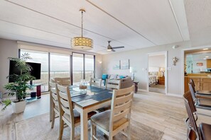 A spacious living area with a dining table, chairs, a ceiling fan, and a large window. - All-suite 3br, Gulf Views: Suntide III - Unit 208 (South Padre Island)