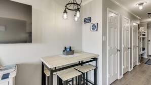 A hallway with a light-colored wall, a hanging light fixture, a small table with stools, and a door with a white frame. - Poolside Vibes, Beach Strolls! Galveston Getaway (Galveston)