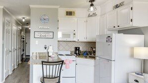 A kitchen with white cabinets, a stove, a microwave, and a refrigerator. There is a clock on the wall and a sign that says 'LIFE HAPPENS THE beach HELPS'. - Poolside Vibes, Beach Strolls! Galveston Getaway (Galveston)