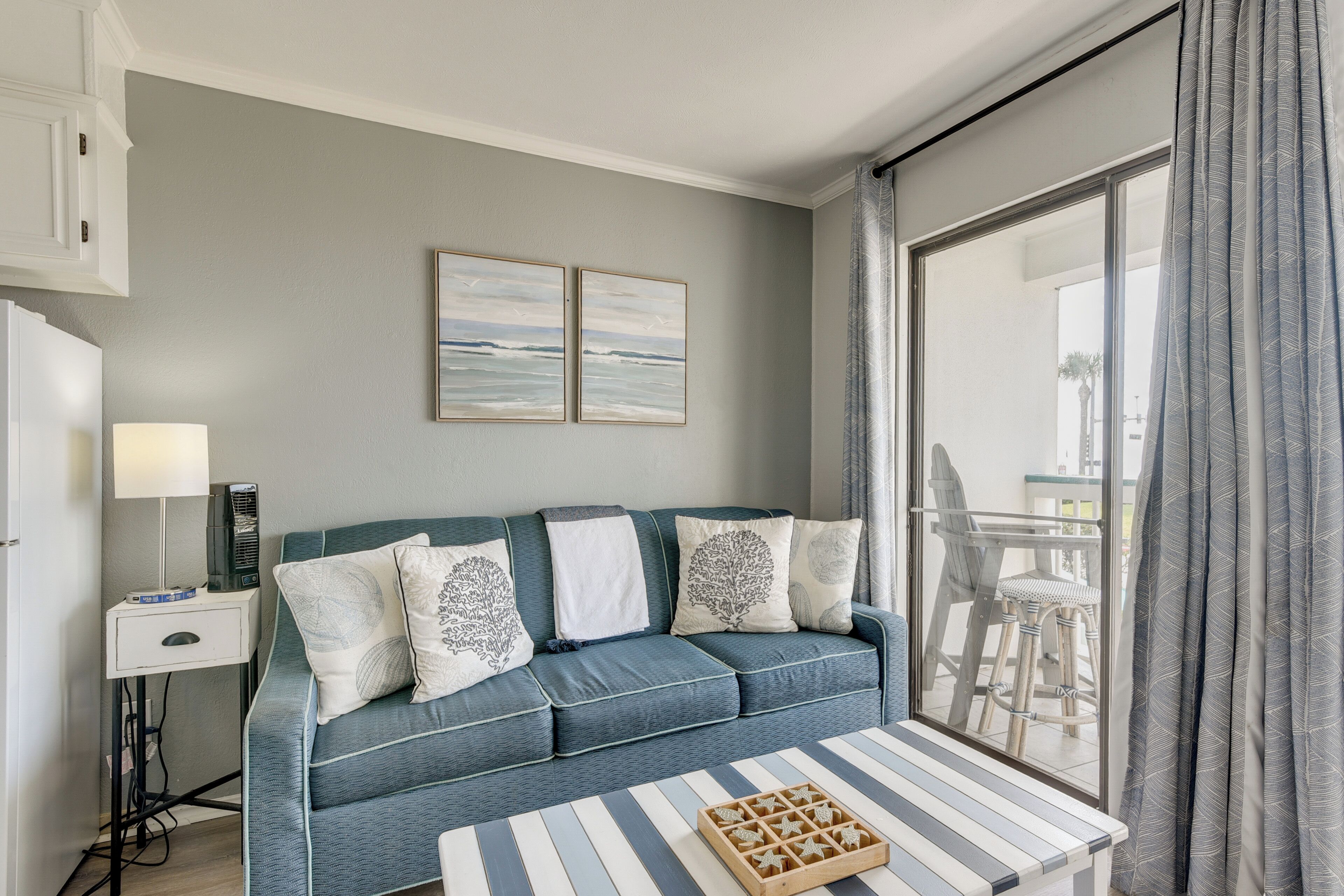 A modern living room with a sofa, a coffee table, and a view of the outdoors through a large window.