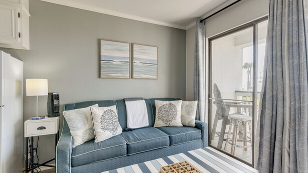 A modern living room with a sofa, a coffee table, and a view of the outdoors through a large window. - Poolside Vibes, Beach Strolls! Galveston Getaway (Galveston)