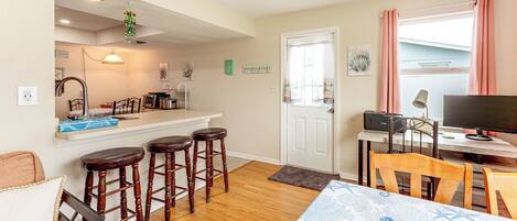 A compact kitchen with a bar area, wooden stools, a dining table with chairs, and a television on a stand.