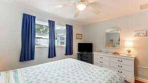 Ein Schlafzimmer mit einem Bett, einem Schminktisch, einem Fernseher und einem Deckenventilator.
