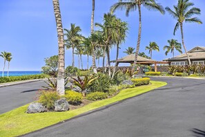A resort with a paved driveway, palm trees, and a view of the ocean. - Halii Kai Condo Close in Proximity to Ocean/pool (Waikoloa)