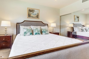 A hotel room with a large bed, two bedside tables, a nightstand, a mirror, and a painting on the wall. - Halii Kai Condo Close in Proximity to Ocean/pool (Waikoloa)