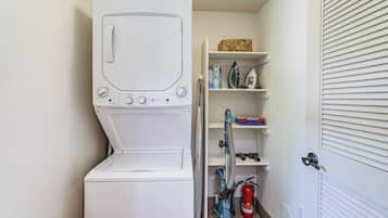 A laundry area with a washing machine and dryer, shelves with cleaning supplies, and a vacuum cleaner.