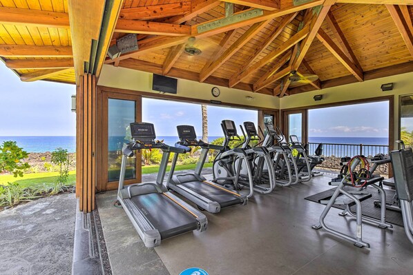 A covered gym area with treadmills and exercise equipment, overlooking a scenic view of the ocean. - Halii Kai Condo Close in Proximity to Ocean/pool (Waikoloa)