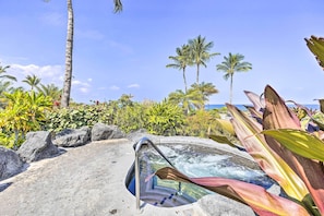 Uma banheira de hidromassagem com vista clara para o oceano, cercada por plantas tropicais e palmeiras.